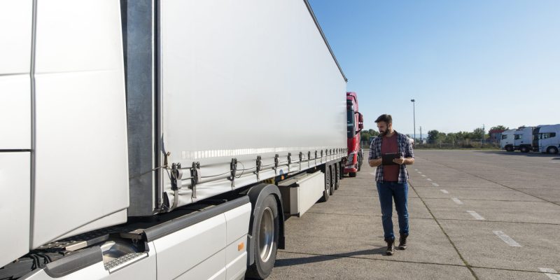 Truck driver inspecting vehicle, trailer and tires before driving.